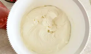 Krem z mascarpone w białej misie, obok miseczka z truskawkami.