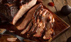 Pokrojona wołowina brisket z ciemną skórką, ułożona na drewnianej desce.