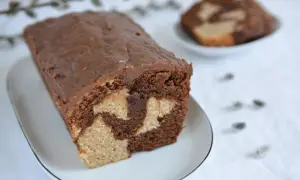 Wilgotna babka marmurkowa z czekoladową polewą na białym talerzyku.