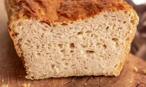 Przekrojony bochenek chleba bezglutenowego na drewnianej desce, z widocznym puszystym wnętrzem.