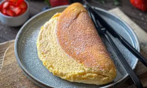 Puszysty omlet na talerzu, posypany cukrem pudrem, obok widelca i noża.