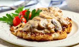 Grillowany kalafior w sosie grzybowym z pomidorkami i natką pietruszki na talerzu.