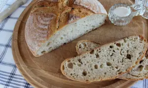 Chleb pszenno-żytni na zakwasie, przekrojony bochenek i kromki na desce.