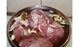 Mięso wieprzowe w zalewie z czosnkiem, liściem laurowym i pieprzem w metalowej misce.
