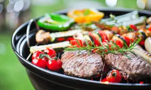 Grill z mięsem, warzywami i ziołami na tle zieleni.