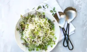 Sałatka coleslaw z kiełkami w białej misce, obok serwetka i łyżki do sałatek.