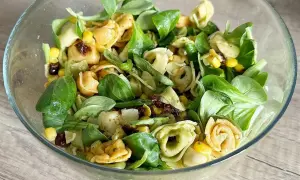 Sałatka z tortellini, kukurydzą, suszonymi pomidorami i zieloną sałatą w szklanej misce.