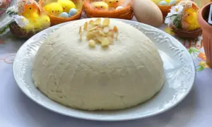 Pascha na białym talerzu, ozdobiona płatkami migdałów, w tle wielkanocne kurczaczki.