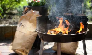 Płonący grill z workami węgla drzewnego w tle.