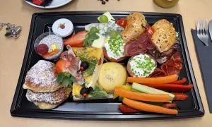 Taca ze śniadaniem kontynentalnym: naleśniki, omlet, sery, wędliny, owoce, warzywa i napój.