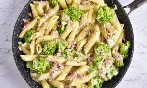 Makaron penne z tuńczykiem i brokułami w kremowym sosie śmietanowo-serowym w czarnej patelni.
