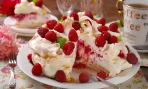 Tort bezowy z bitą śmietaną, malinami i listkami mięty na białym talerzu.