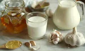 Mleko, miód i czosnek na marmurowym blacie.