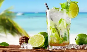 Szklanka orzeźwiającego mojito z limonką i miętą na tle plaży.