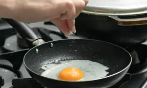 Ręka posypuje solą jajko sadzone smażone na patelni.