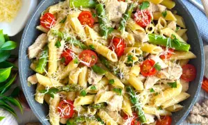 Makaron penne z kurczakiem, szparagami i pomidorkami koktajlowymi, posypany serem.