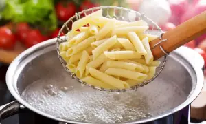 Makaron penne w cedzaku nad garnkiem z gotującą się wodą.