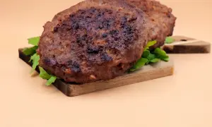 Dwa soczyste kotlety z wołowiny, idealne do burgerów, leżą na desce z rukolą. Prosty przepis na to, jak zrobić kotlety z wołowiny.
