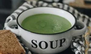 Zielony kremowy zupa w misce z napisem "SOUP". Idealna do mrożenia zup, by cieszyć się smakiem przez cały rok. Obok kromka chleba.