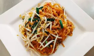 Pad thai z kiełkami fasoli mung, szczypiorkiem i orzeszkami ziemnymi na białym talerzu.