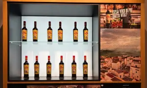 Butelki likieru Amaro Lucano ustawione na półkach, obok opisu produktu i włoskiego krajobrazu.