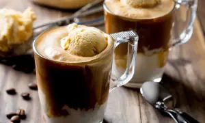 Dwa kubki affogato z lodami waniliowymi i kawą, na drewnianym stole z ziarnami kawy.