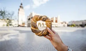 Dłoń trzyma obwarzanka krakowskiego z makiem na tle Sukiennic.