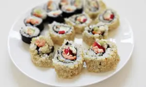 Talerz z rolkami sushi uramaki, niektóre obtoczone w sezamie, z widocznym łososiem i warzywami.