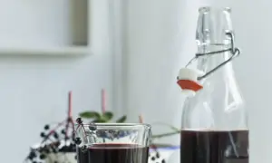 Szklanka i butelka z ciemnym sokiem z czarnego bzu, ozdobione gałązkami z owocami.