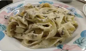 Pappardelle z kremowym sosem, w którym wyczuwalne są kawałki trufli. Makaron z pastą truflową i śmietaną wygląda apetycznie.