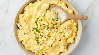 Kremowa pasta jajeczna z posiekanym szczypiorkiem w misce, z drewnianą łyżką.
