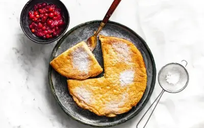 Puszysty omlet posypany cukrem pudrem, podany z żurawiną i łyżką.
