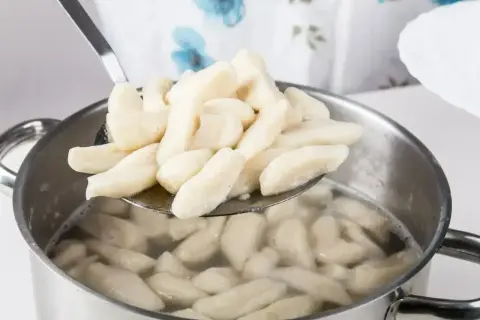 Kopytka gotujące się w garnku, wyjmowane łyżką cedzakową.