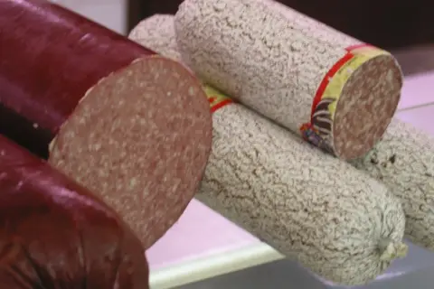 Kawałki ciemnej i jasnej kiełbasy salami, jedna przekrojona.