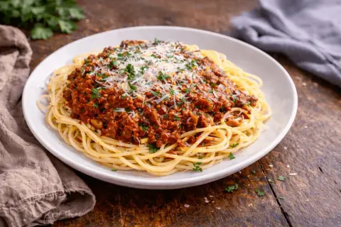 Talerz spaghetti z sosem bolońskim, posypany parmezanem i natką pietruszki.
