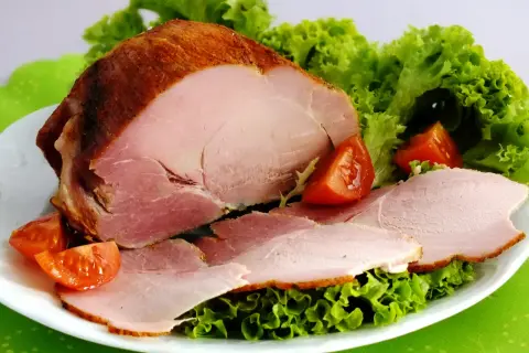 Pieczona szynka peklowana z sałatą i pomidorkami na białym talerzu.