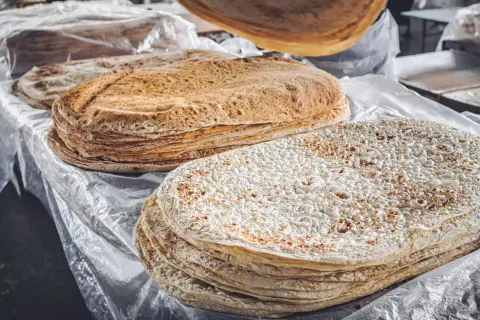 Stos cienkich, okrągłych placków lawaszu na stole, niektóre z nich lekko przypieczone.