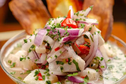 Ceviche z ryby, cebuli, papryczki chili i kolendry w szklanej misce, z chipsami bananowymi w tle.