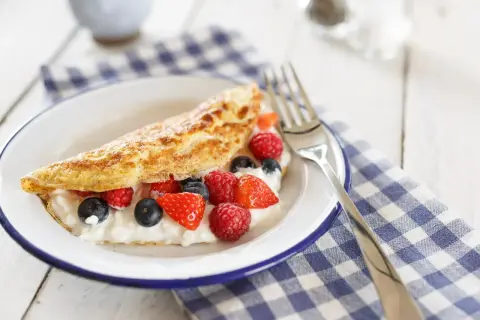 Puszysty omlet z serkiem i owocami leśnymi na talerzu.