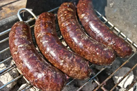 Cztery soczyste kaszanki z grilla pieką się na ruszcie, uwalniając apetyczny aromat.