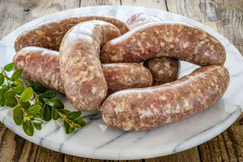 Surowa kiełbasa na marmurowej desce, gotowa do przyrządzenia. Zastanawiasz się, ile czasu parzyć surową kiełbasę?