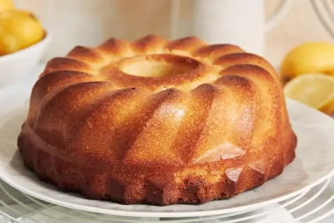 Puszysta babka z wgłębieniem pośrodku, na talerzu, z cytrynami w tle.