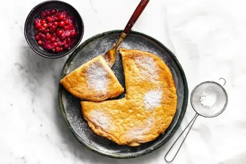 Puszysty omlet posypany cukrem pudrem, podany z żurawiną i łyżką.