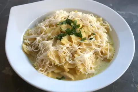 Szybki obiad z twarogiem: makaron farfalle w kremowym sosie, posypany startym serem i natką pietruszki.
