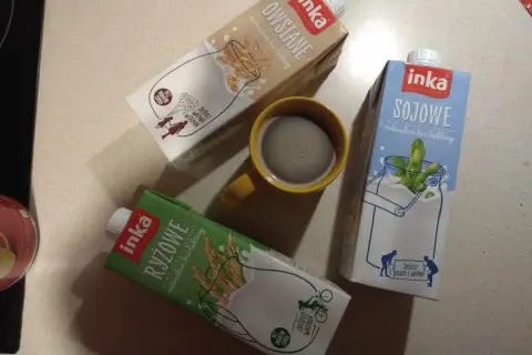 Trzy kartony napojów Inka (owsiane, sojowe, ryżowe) i kubek kawy.