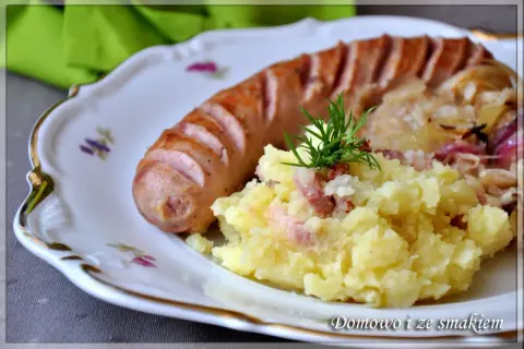 Biała kiełbasa z ziemniakami i kapustą kiszoną, udekorowana koperkiem.