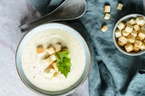 Kremowa zupa z kalarepy z grzankami i natką pietruszki na niebieskim tle.