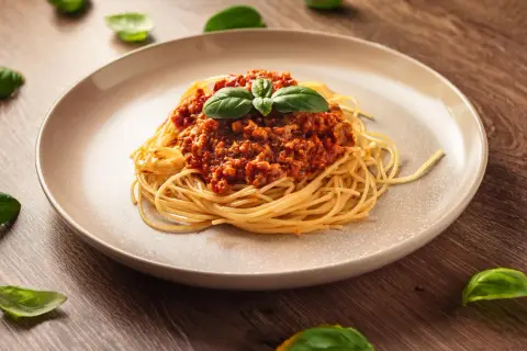 Talerz spaghetti z sosem bolońskim i listkami bazylii na drewnianym tle.