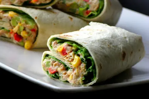 Tortilla z tuńczykiem, kukurydzą, papryką i sałatą na białym talerzu.