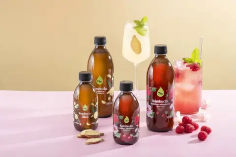 Butelki z kombuchą, drinki, maliny i imbir na różowym tle.